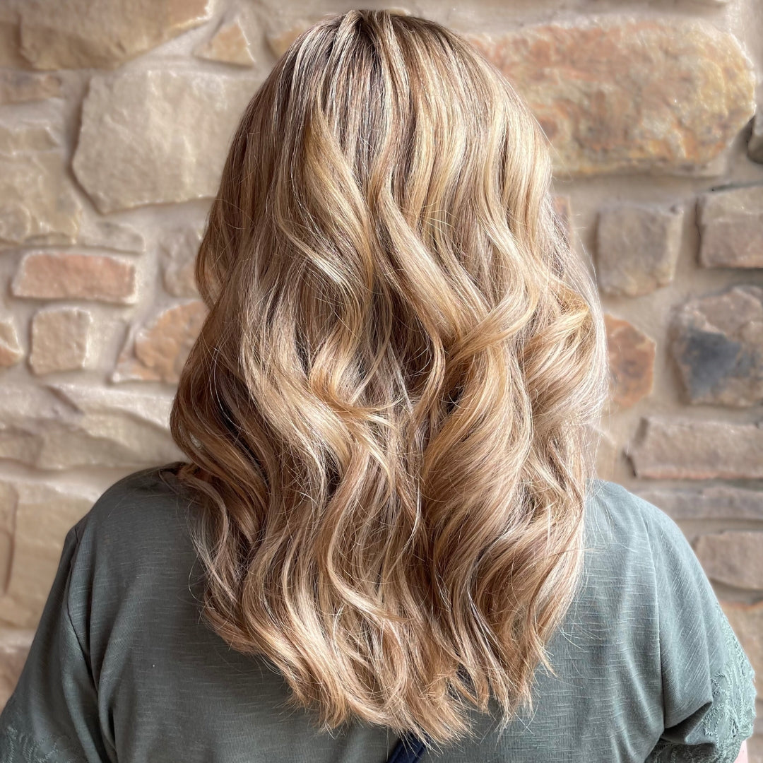 This is an image of one of Ippodaro Natural Salon’s customers moments after a stylist finished their color services. This image showcases a beautiful blonde, standing in front of a rock wall. We see the back of her hair, to really admire her new blonde highlights. She is standing in front of a rock wall (which is slightly out of focus).