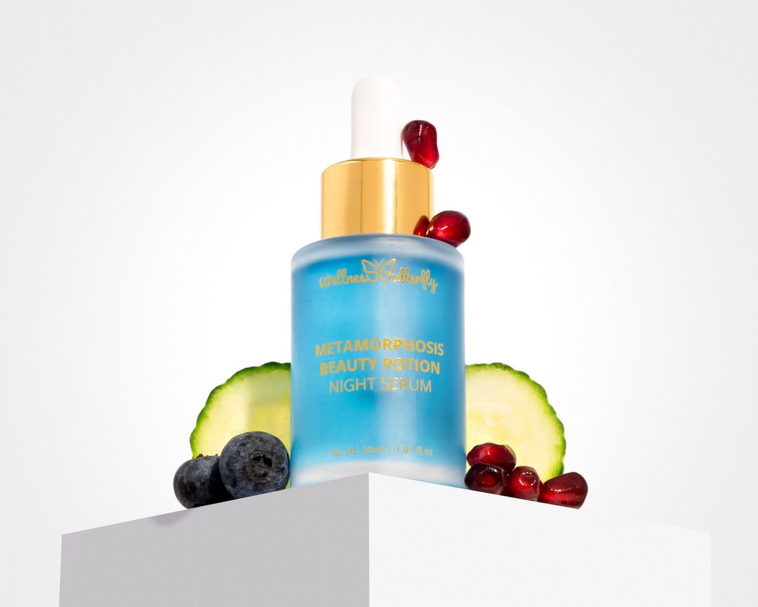 Wellness Butterfly Skincare Matamorphosis Night Serum 1.01oz. White background with cucumbers, blueberry, and pomegranate seed. Clear glass bottle, with gold lettering. Light blue serum. White, gold dropper. At Ippodaro Natural Salon, TX