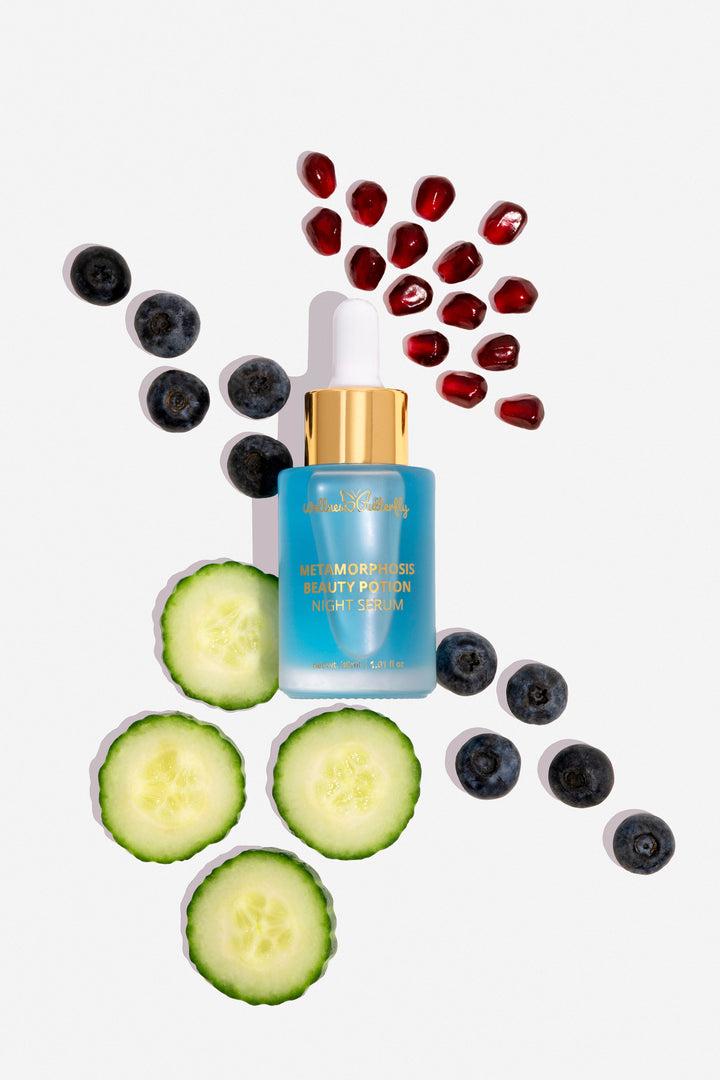 Wellness Butterfly Skincare Matamorphosis Night Serum 1.01oz. White background with cucumbers, blueberry, and pomegranate seed. Clear glass bottle, with gold lettering. Light blue serum. White, gold dropper. At Ippodaro Salon, San Antonio, TX